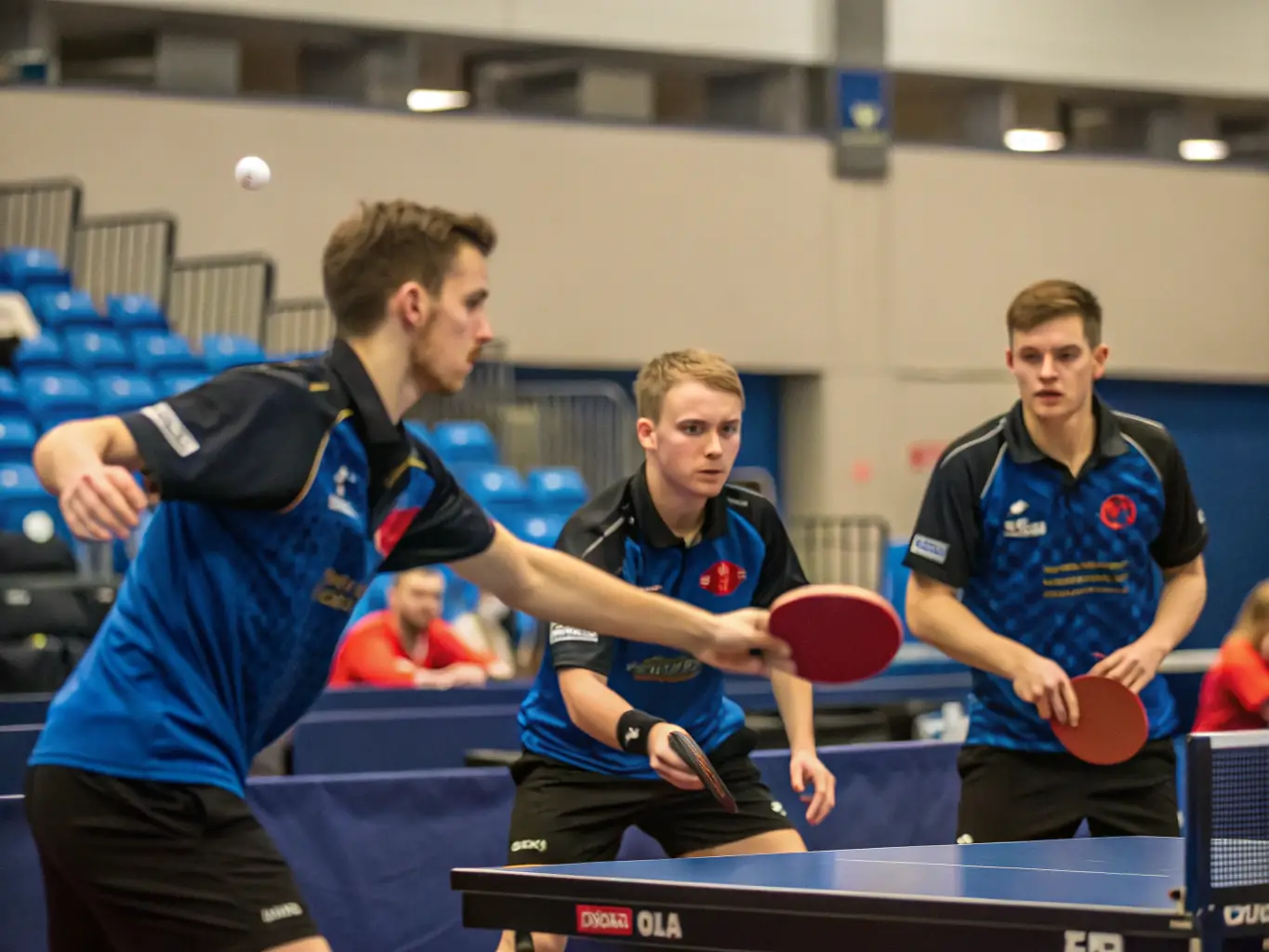 A vibrant image showing members of GAILLON AUBEVOYE TENNIS DE TABLE actively engaged in a friendly table tennis match, set in a well-lit gymnasium with club banners visible in the background.